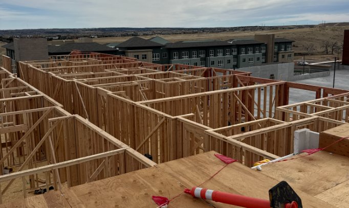 Interior wall framing on a Wood Framers jobsite with a completed multifamily building in the background