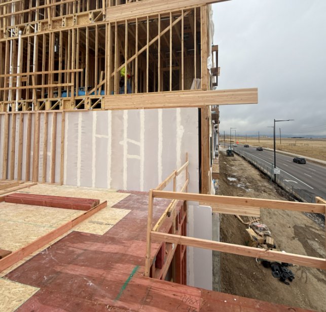 Exterior wall framing at a multifamily wood-frame construction site with a Colorado roadway in the background