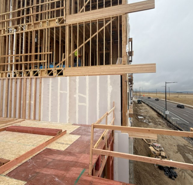 Wood-frame multifamily building under construction along a Colorado roadway